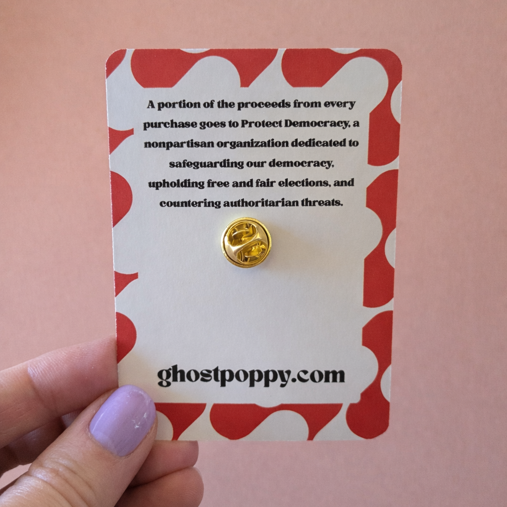 Gold pin on a card with 'ghostpoppy.com' branding against a pink background