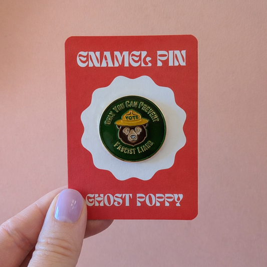 Enamel pin on a red card held by a hand against a pink background