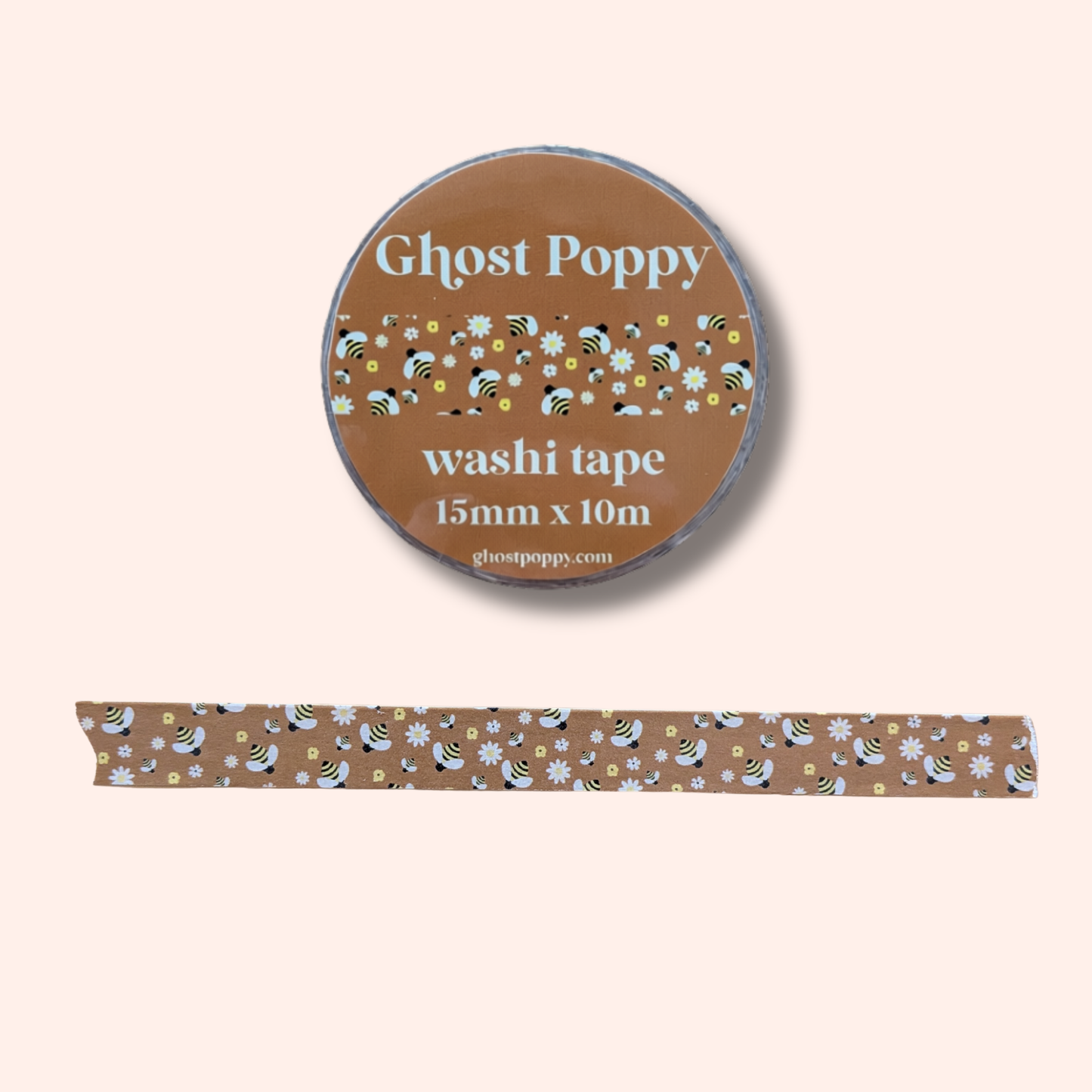 Buzzin Washi Tape by Ghost Poppy is a brown roll of washi tape crafted from rice paper, featuring a charming floral and bee pattern. Displayed with a strip of the tape below on a light beige background, it’s perfect for adding a whimsical touch to your journaling projects.