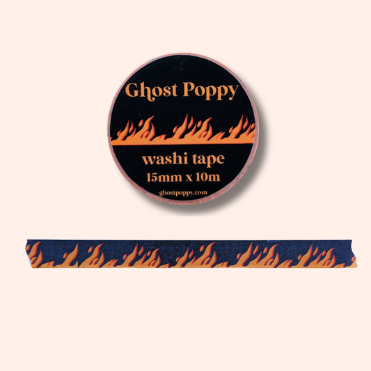 A roll of Road to Hell Washi Tape by Ghost Poppy, crafted from premium rice paper, features a striking black background with an orange flame design. Perfect for journaling or crafts, a strip of the tape—highlighting the same vibrant flame pattern—is displayed below the roll.