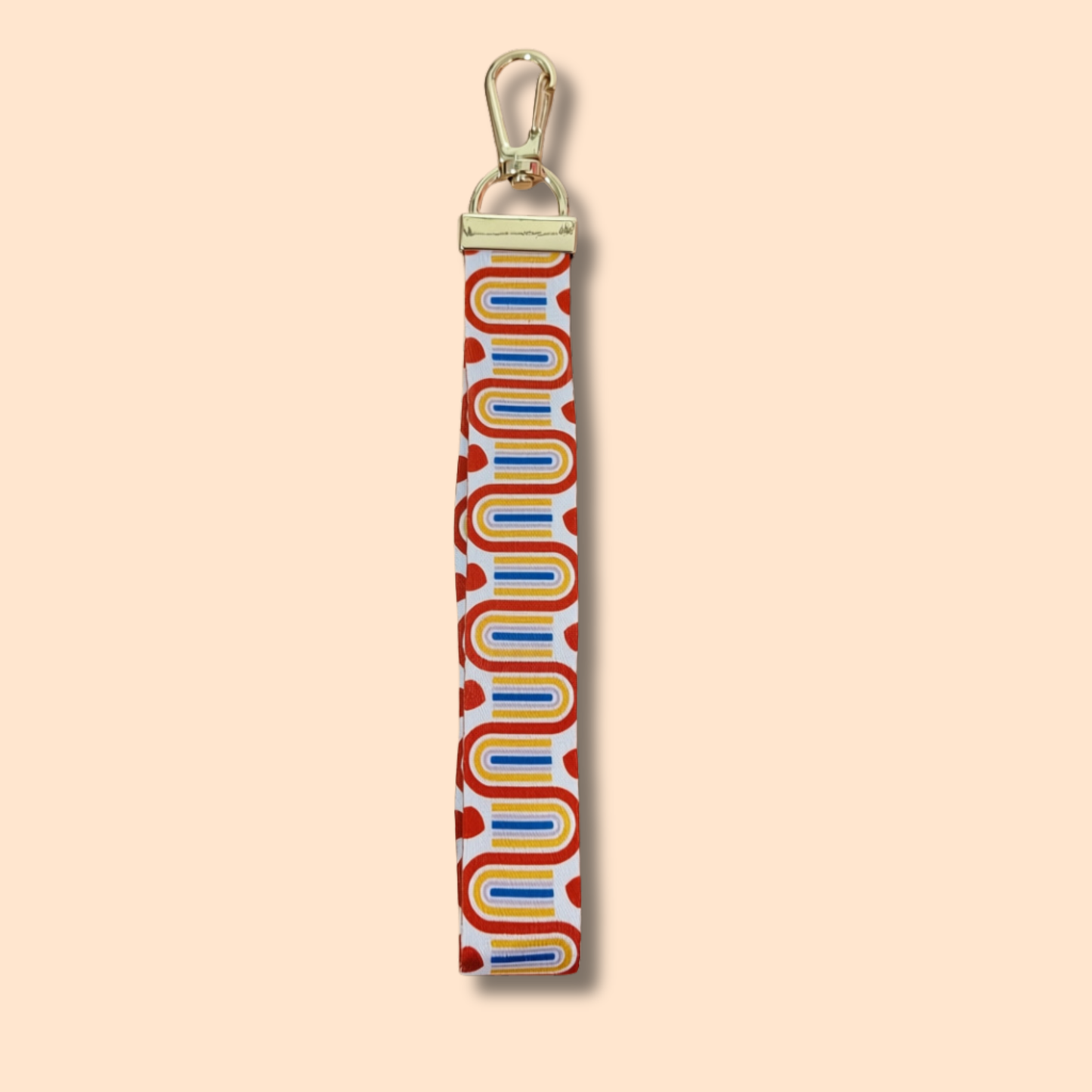 Introducing the Rainbow Wristlet Lanyard Keychain by Ghost Poppy—a stylish accessory featuring a gold lobster clasp and a durable fabric strap. The retro wavy pattern in yellow, blue, and red is accented with red heart shapes on a white background, all set against a beige backdrop. This vibrant keychain adds a playful touch to your everyday essentials.