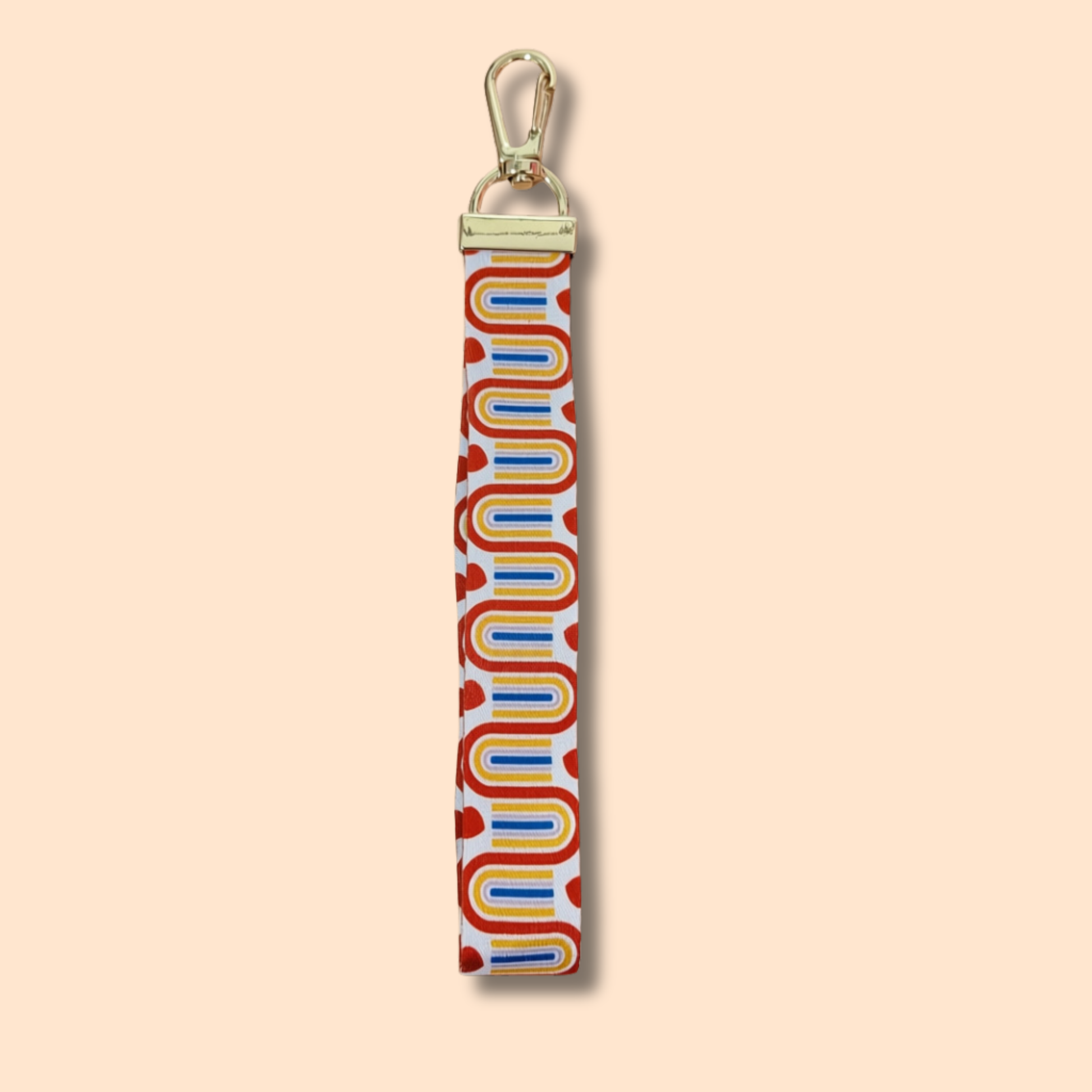Introducing the Rainbow Wristlet Lanyard Keychain by Ghost Poppy—a stylish accessory featuring a gold lobster clasp and a durable fabric strap. The retro wavy pattern in yellow, blue, and red is accented with red heart shapes on a white background, all set against a beige backdrop. This vibrant keychain adds a playful touch to your everyday essentials.