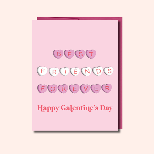 The Best Friends Forever – Valentine’s Galentine’s Day Card by Ghost Poppy showcases candy hearts spelling out “Best Friends Forever” on a pink card, with “Happy Galentines Day” in red text at the bottom. This blank greeting card is printed on quality cardstock and displayed against a light pink background.