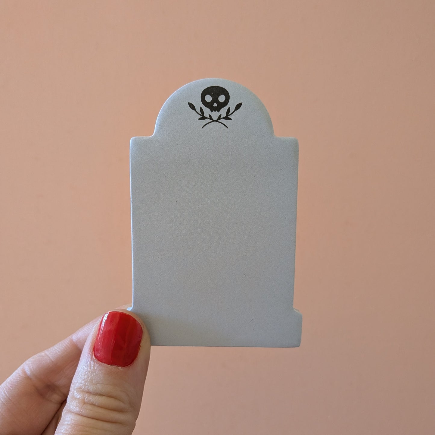 A hand holds a 3x2 inch tombstone-shaped Mini Memento Mori Sticky Note by Ghost Poppy, featuring a black skull and leaf icon at the top.