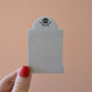 A hand holds a 3x2 inch tombstone-shaped Mini Memento Mori Sticky Note by Ghost Poppy, featuring a black skull and leaf icon at the top.