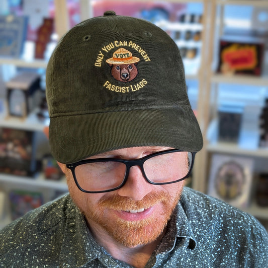 A person wears a dark green Ghost Poppy Only You Corduroy Hat featuring a bear in a park ranger hat and the text Only you can prevent fascist liars.