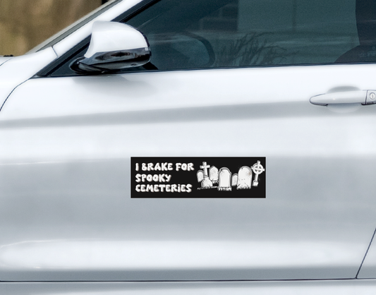 A rectangular I Brake For Spooky Cemeteries Car Magnet on a silver car door, featuring the text I BRAKE FOR SPOOKY CEMETERIES next to a graphic of tombstones.