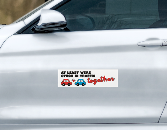 Ghost Poppy Stuck In Traffic Car Magnet featuring a red car and a blue car separated by a small heart with the text At least we’re stuck in traffic together.