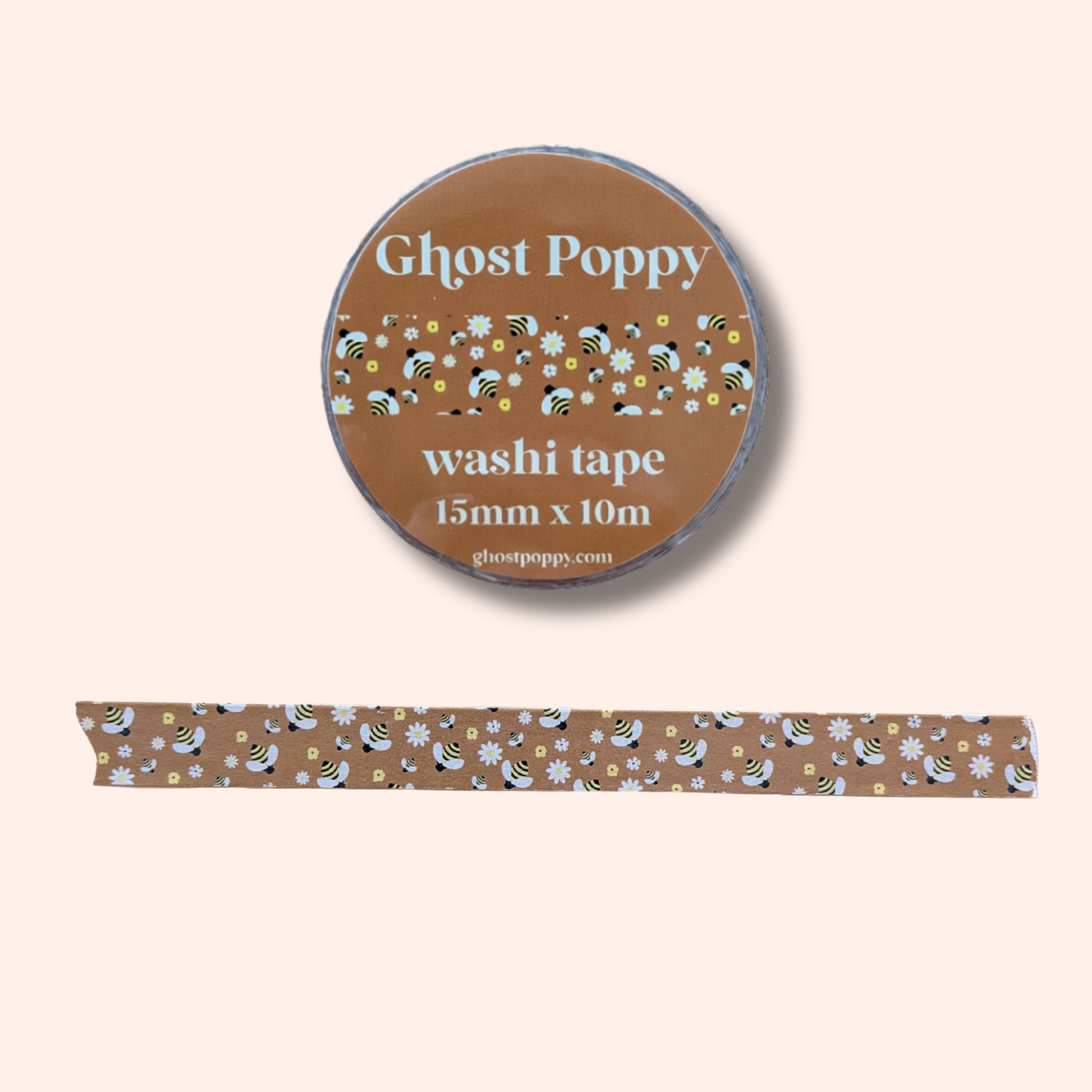Buzzin Washi Tape by Ghost Poppy is a brown roll of washi tape crafted from rice paper, featuring a charming floral and bee pattern. Displayed with a strip of the tape below on a light beige background, it’s perfect for adding a whimsical touch to your journaling projects.